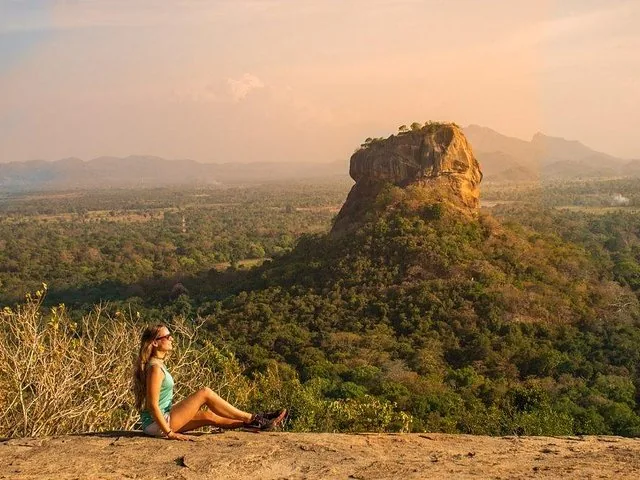 A woman sitting relaxed on a rock overlooking Sigiriya and the surrounding landscape.