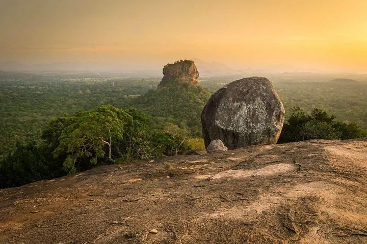 Una gran formación rocosa cerca del borde de un acantilado con Sigiriya en la distancia.